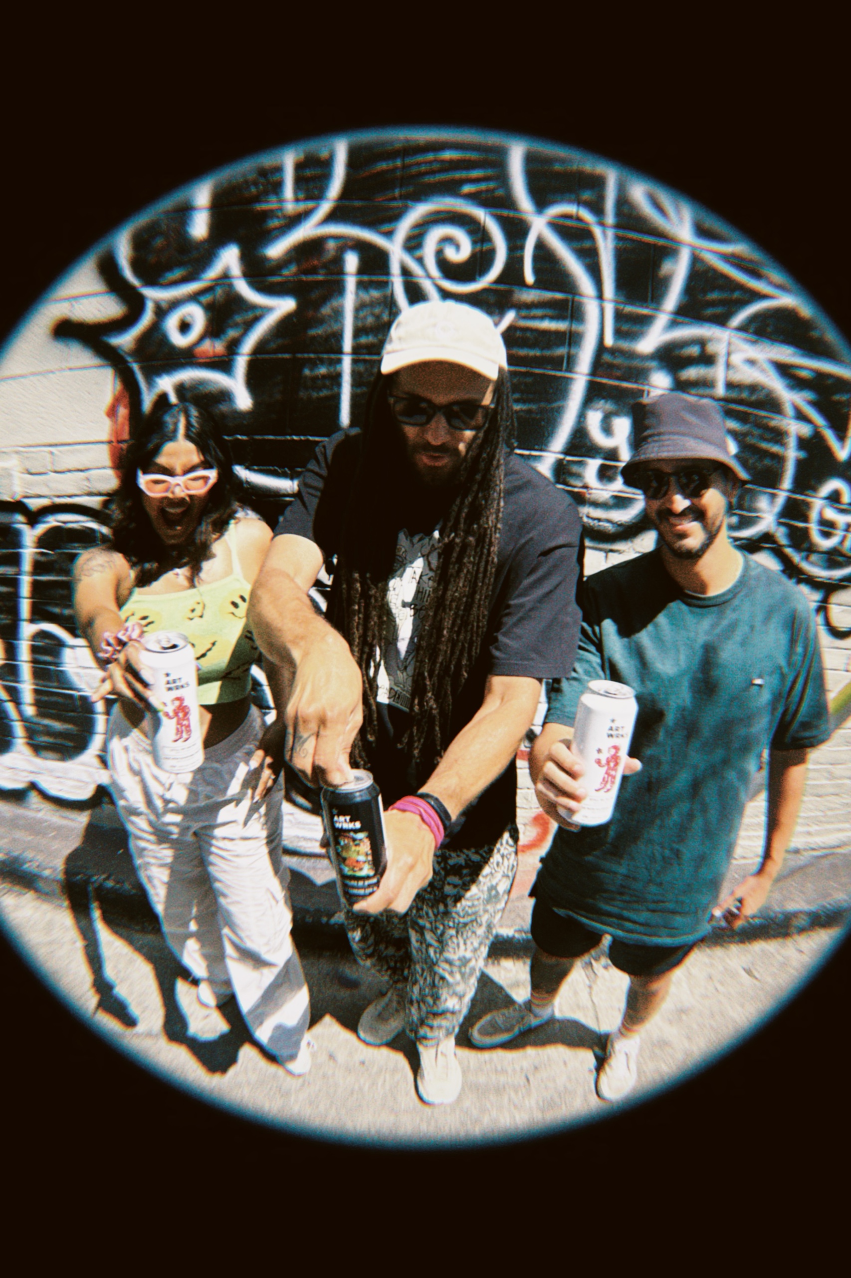 Fisheye photograph of three friends holding ART WRKS cans in front of a black-and-white mural.