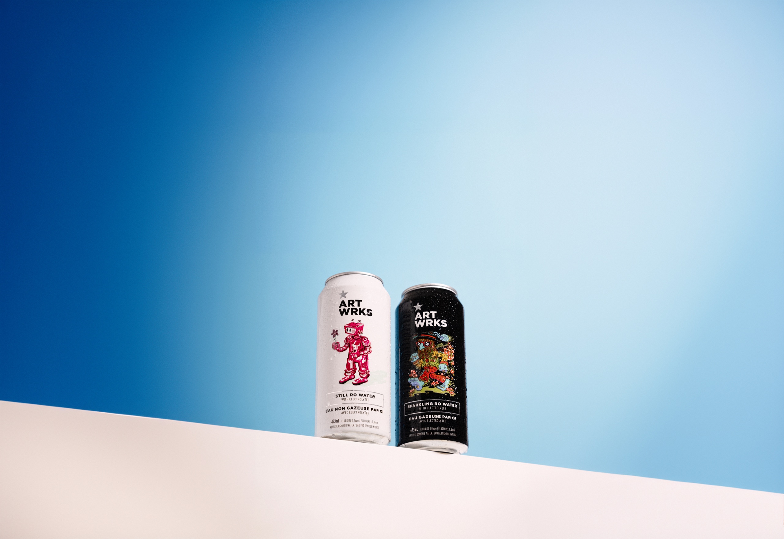 White and black ART WRKS cans on a sloping white surface against a blue studio background.