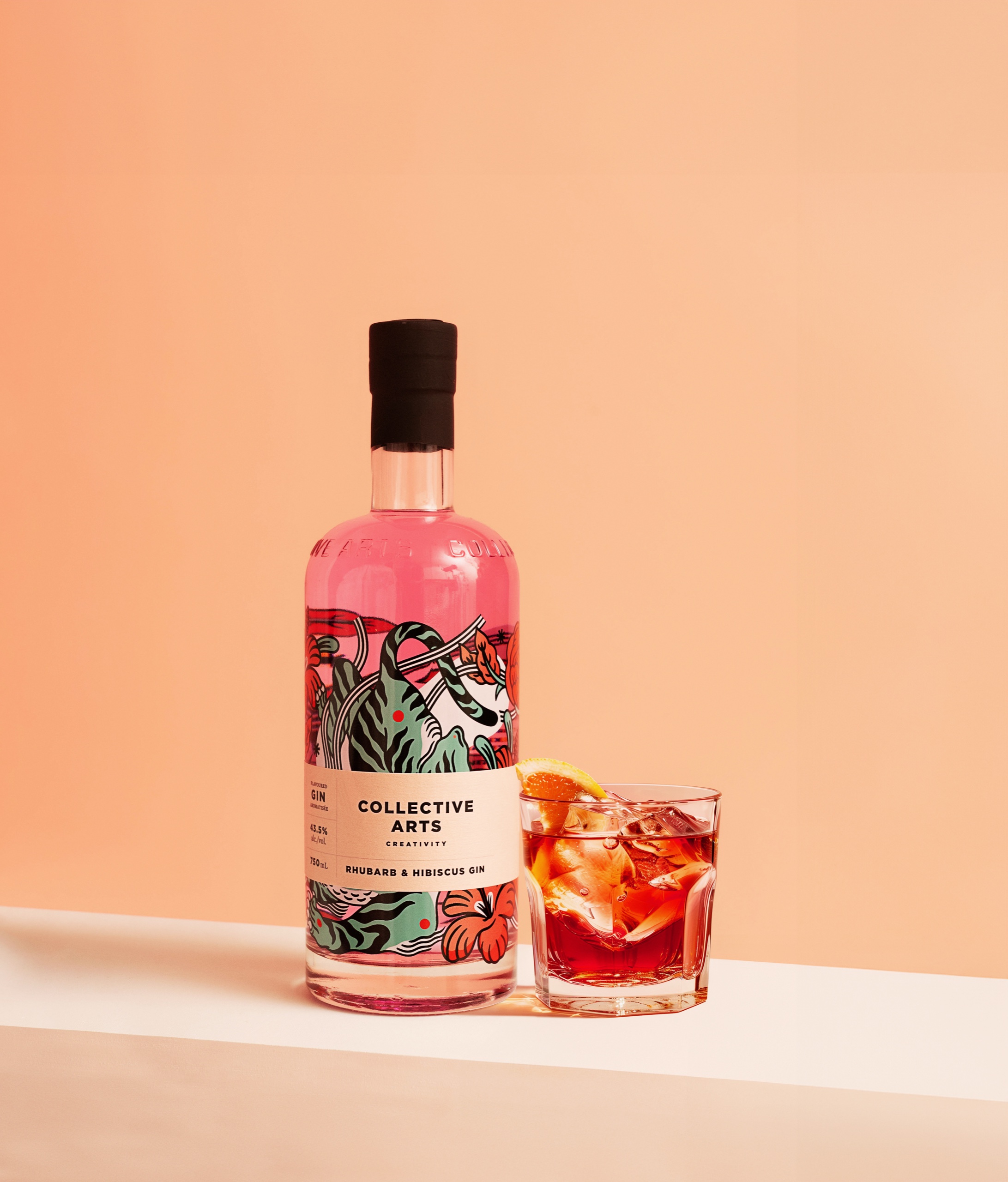 Collective Arts rhubarb and hibiscus gin beside a Negroni with an orange garnish against peach.