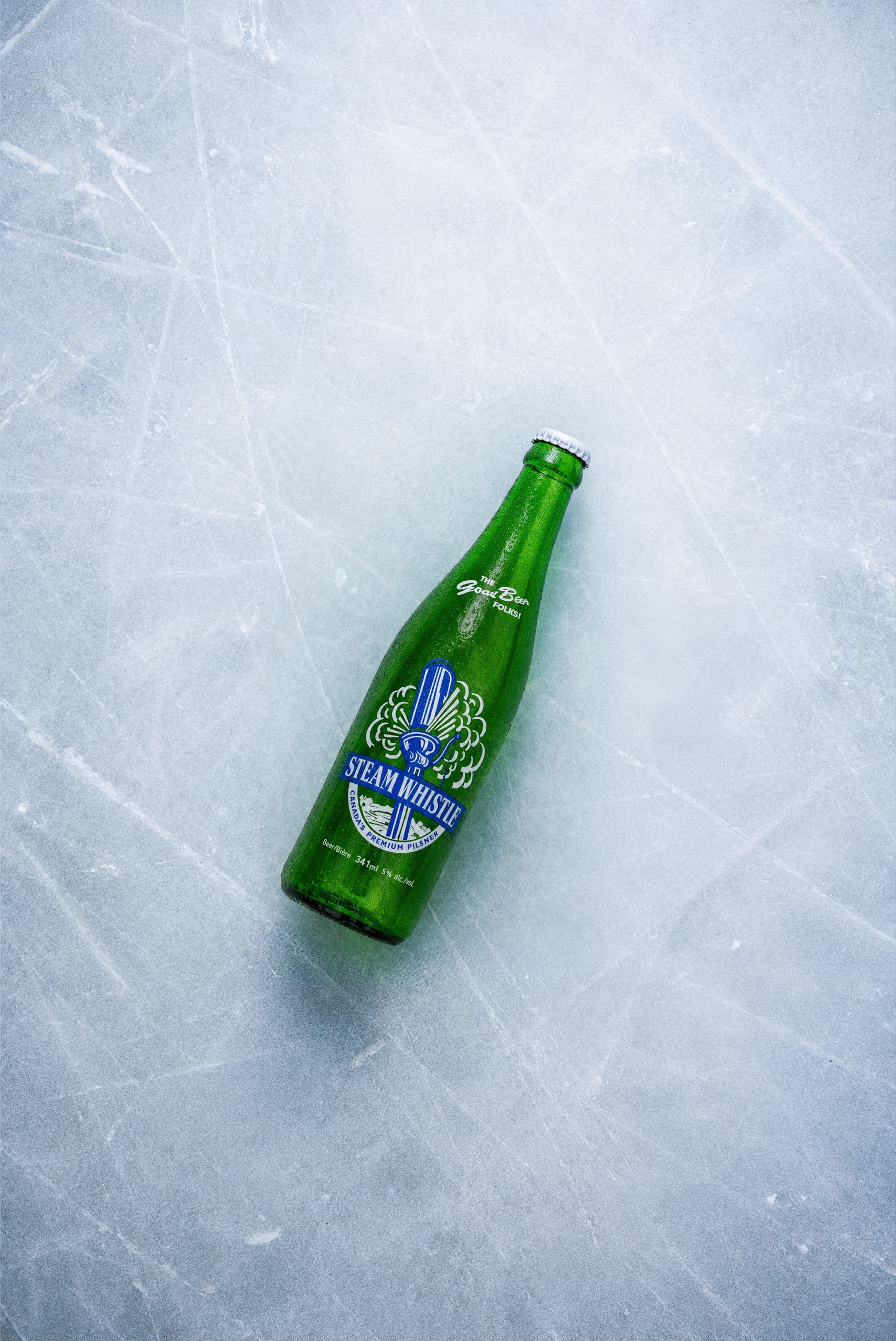 A green Steam Whistle bottle lying diagonally on textured ice.