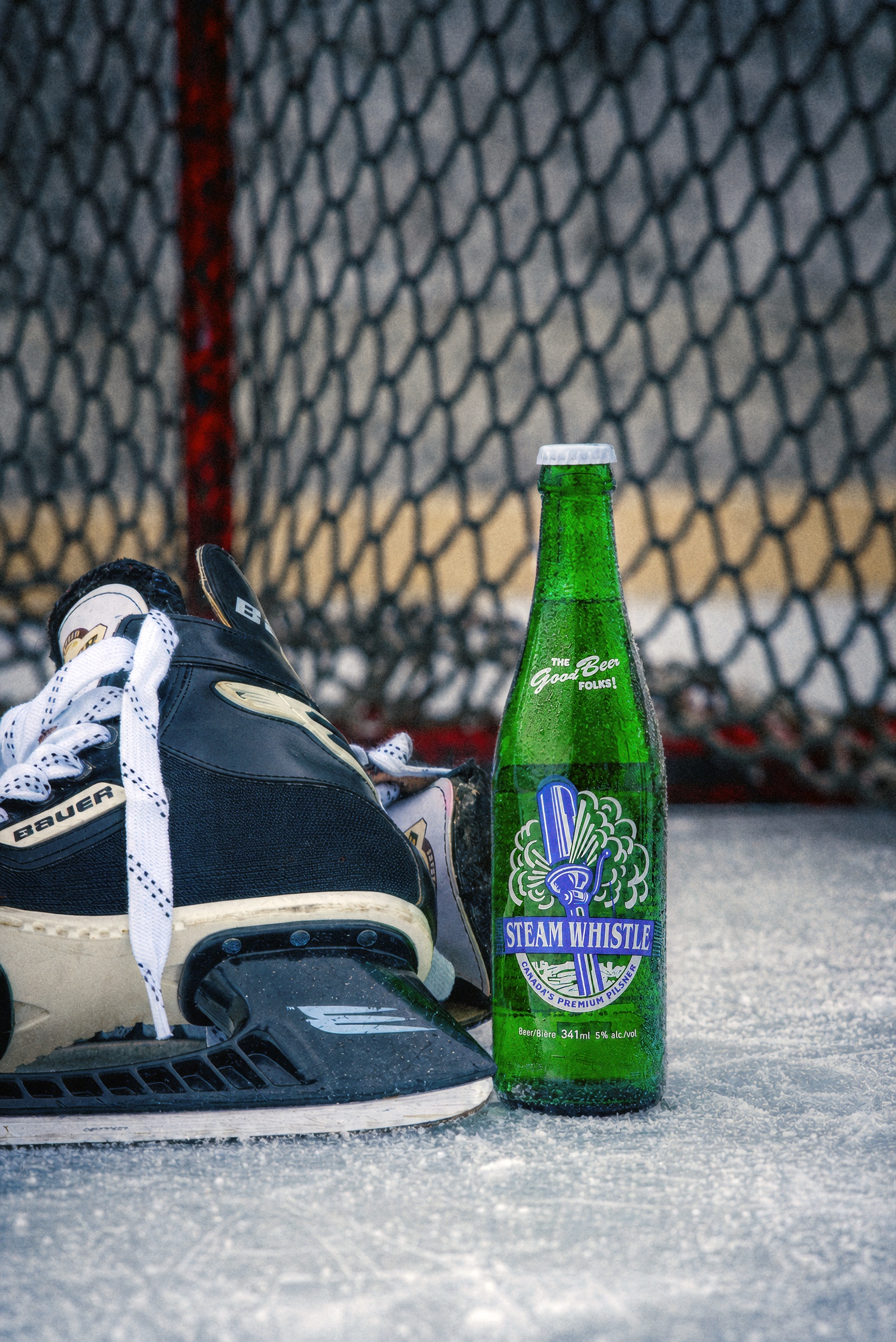 A green Steam Whistle bottle beside hockey skates on the ice in front of a goal.
