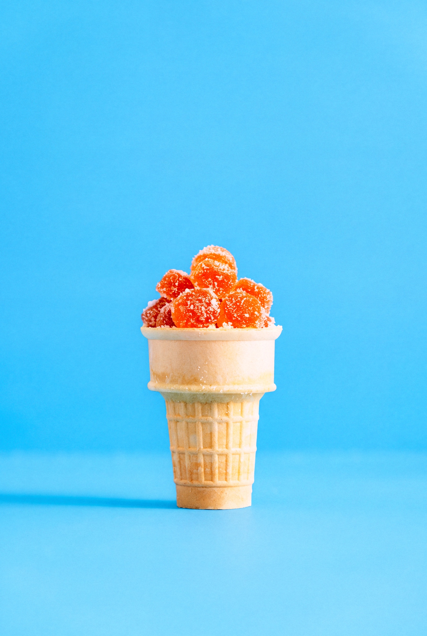 Sugar-coated Collective Project Squeezies gummies piled in a flat-bottomed ice cream cone against blue.
