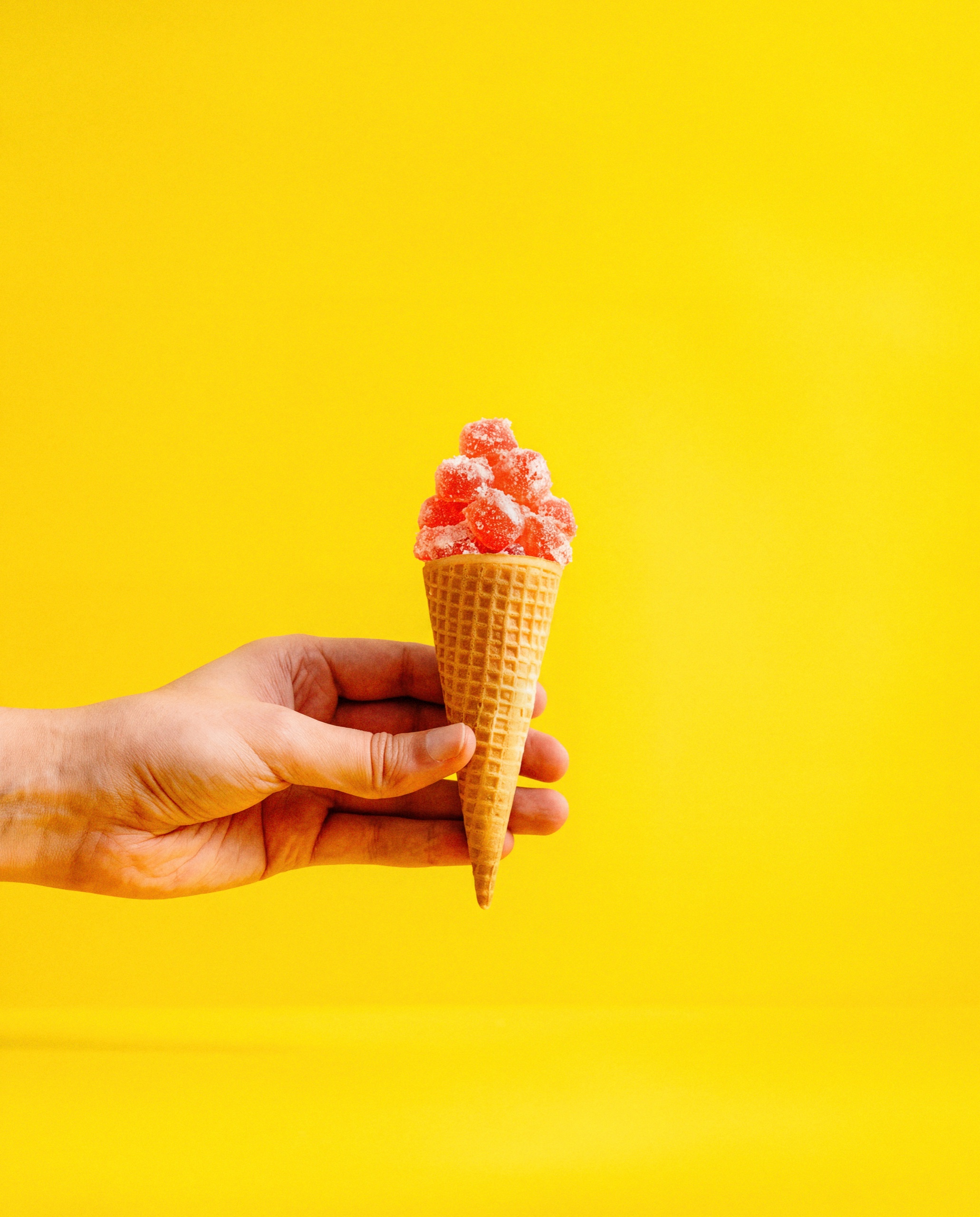 A hand holds a waffle cone filled with Collective Project Squeezies gummies against a bright yellow background.