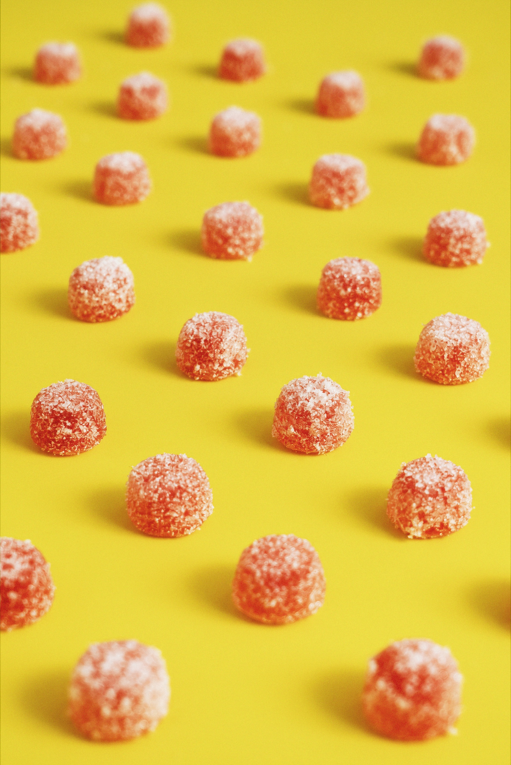 Rows of sugar-coated pink Collective Project Squeezies gummies arranged across a bright yellow background.