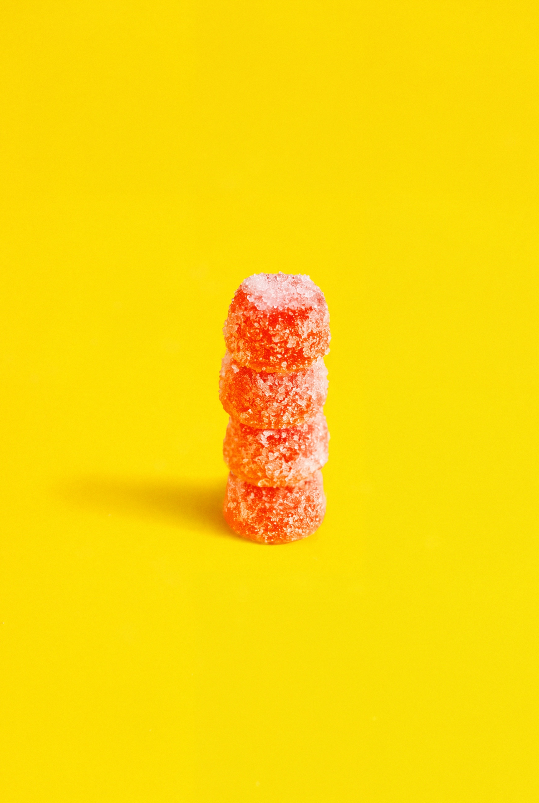 Four sugar-coated pink Collective Project Squeezies gummies stacked against a yellow background.