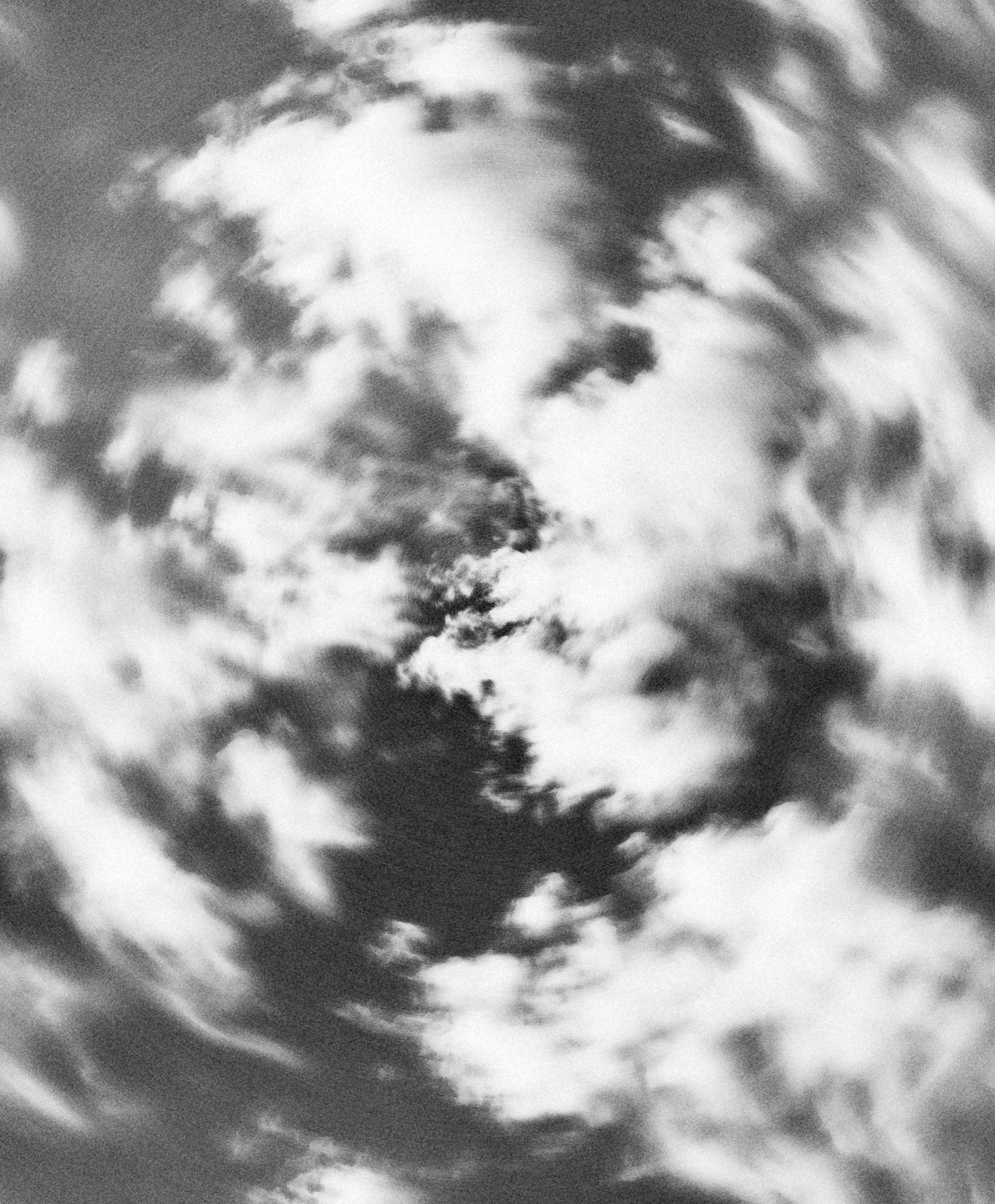 Swirling cloud shapes captured with motion blur in a grainy black-and-white sky.
