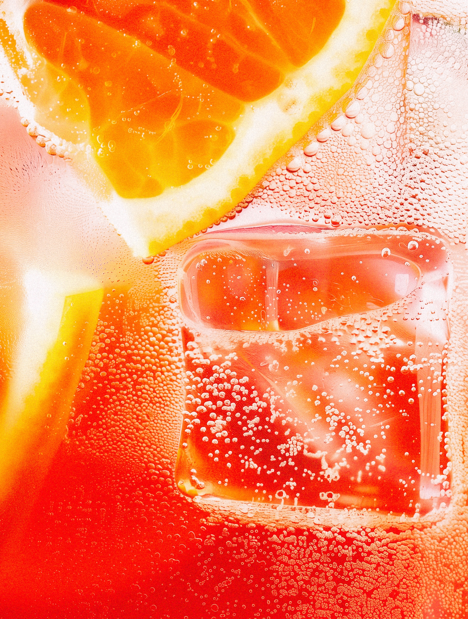 Close-up of orange slices, clear ice and sparkling bubbles in an orange-red drink.