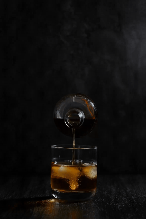 An animated loop of rye pouring from a bottle into a glass with ice against a dark background.