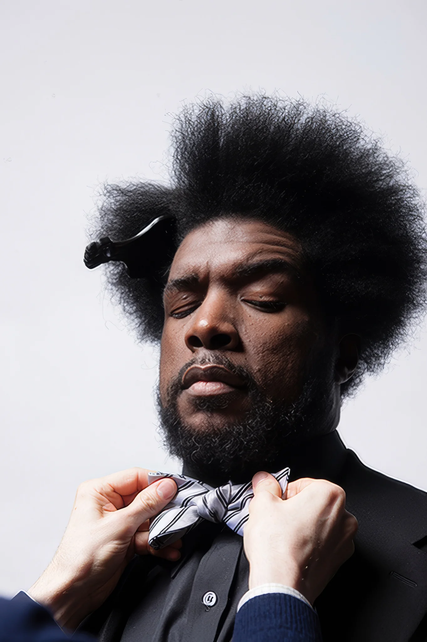 Colour studio portrait of a man with an afro having his patterned bow tie adjusted.