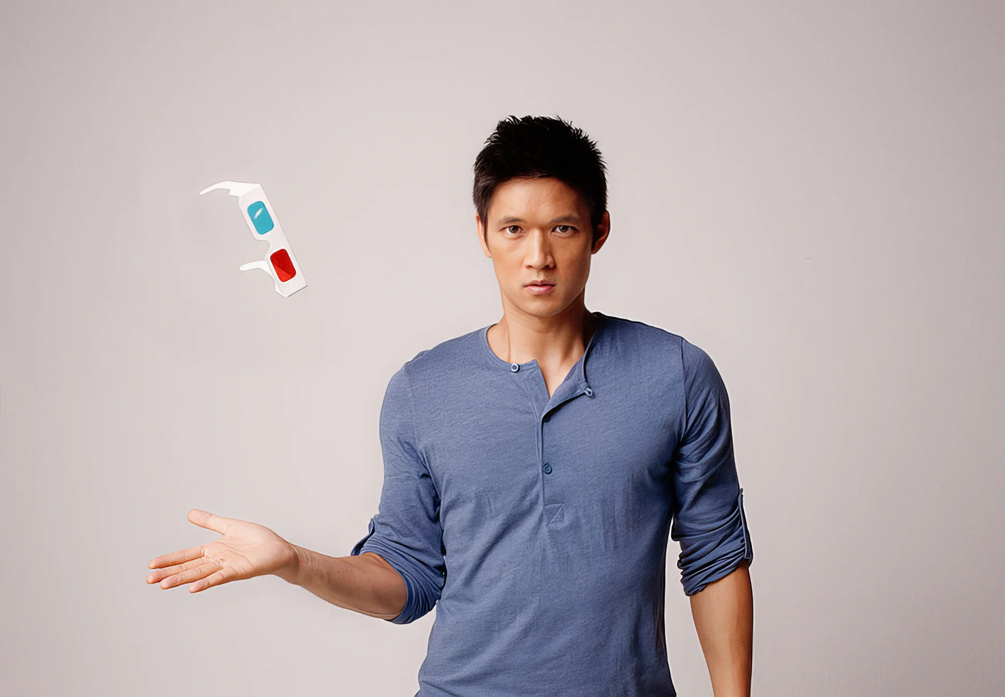 A man in a blue shirt tosses white 3D glasses above his open hand.