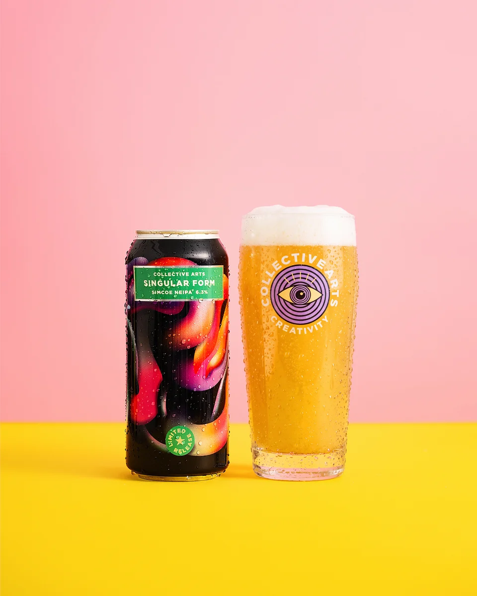 Collective Arts Singular Form can and a glass of golden beer on a yellow surface against a pink background.