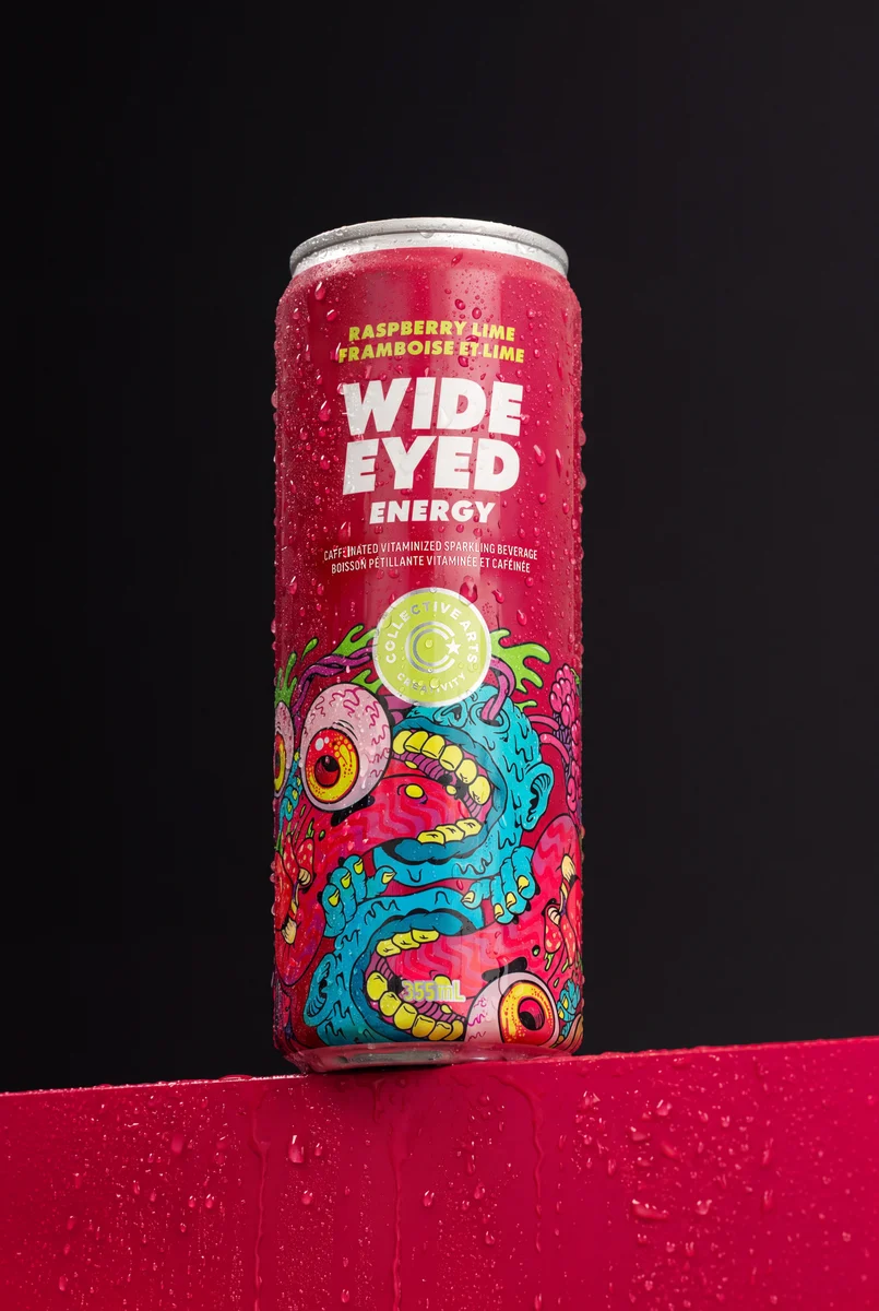 Pink Wide Eyed Raspberry Lime Energy can covered in condensation on a red plinth against a dark background.